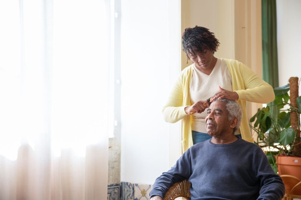 A caregiver gently helping an older man near a sunlit window